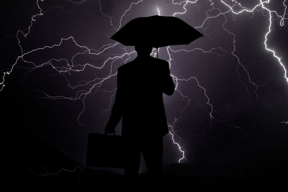 A businessman holding an umbrella during a lightning storm