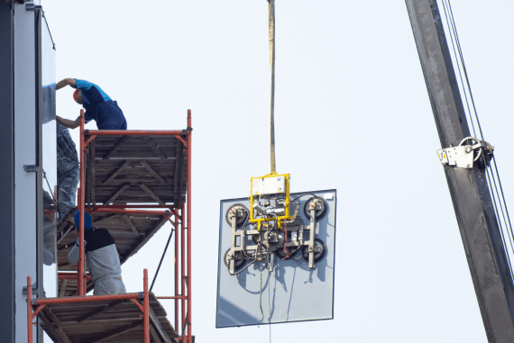 A mechanical lifting aid hoisting a glass panel up a tall building